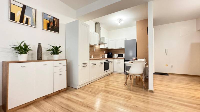 Küche in einer 2-Zimmer-Wohnung mit weißen Schränken und einem Boden in Holzoptik.