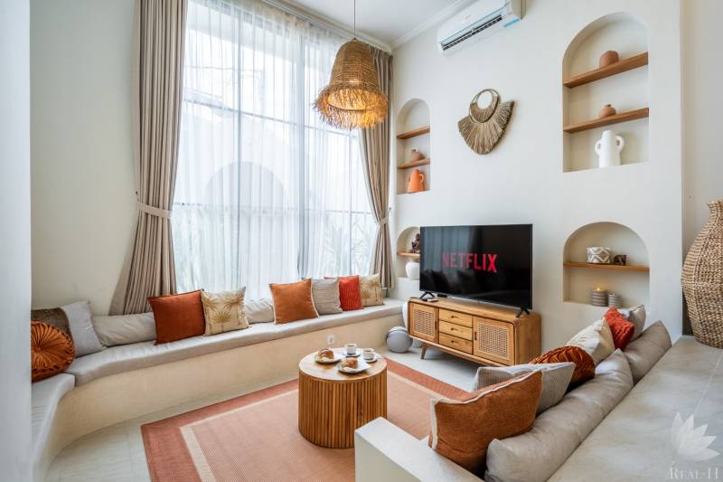 Helles Wohnzimmer in der Villa mit Sofa, Fernseher und dekorativer Beleuchtung.