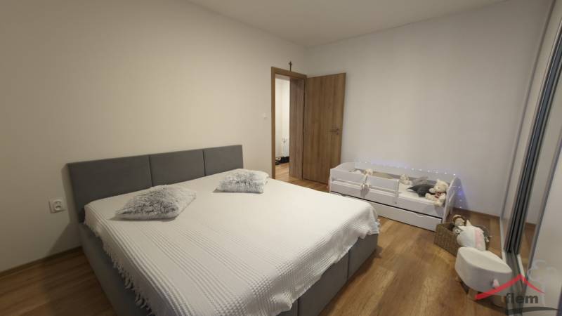 Schlafzimmer mit grauem Bett und Kinderbett, Holzboden in einer 2-Zimmer-Wohnung.