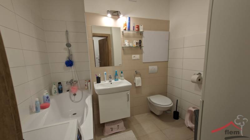 Badezimmer in einer 2-Zimmer-Wohnung mit Badewanne, Waschbecken, Spiegel und heller Wandverkleidung.