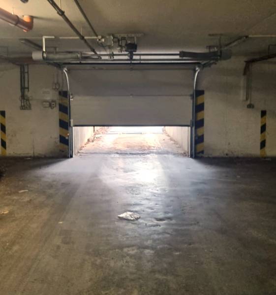 Das halb geöffnete Garagentor führt nach draußen, die Umgebung ist von indirektem Licht beleuchtet.