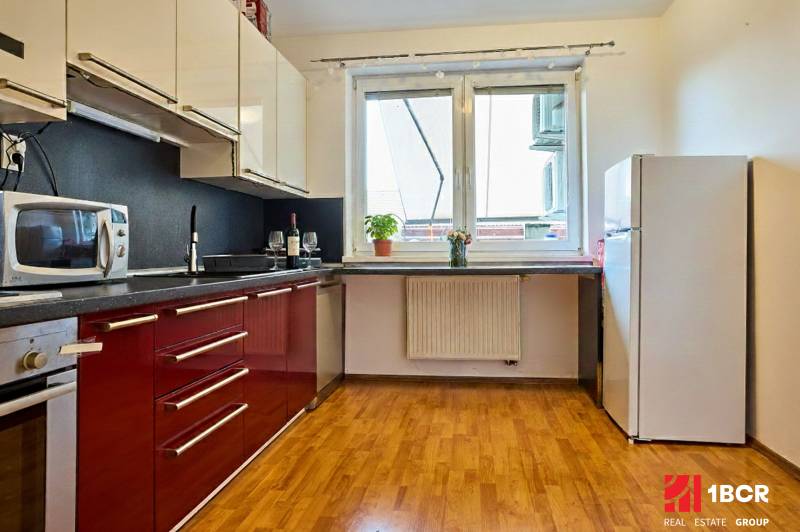 Küche in einer 2-Zimmer-Wohnung mit roten Schränken und einem Boden in Holzoptik.