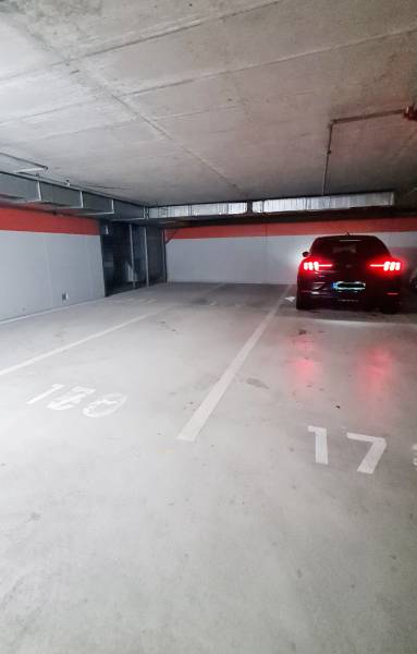 Unterirdische Garage mit Auto, leerem Parkplatz und Betonwänden.