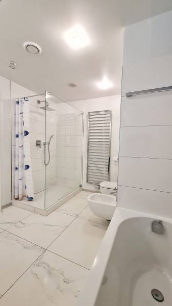Badezimmer mit Badewanne, Dusche und Toilette in einer 3-Zimmer-Wohnung. Weiße Fliesen.