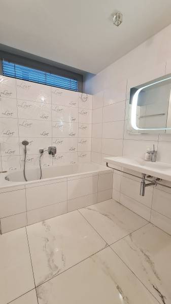 Badezimmer mit Badewanne und Fliesen in einer 3-Zimmer-Wohnung, weiße und graue Farbtöne.