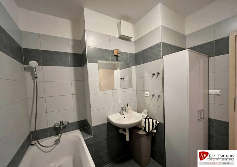 Badezimmer in einer 2-Zimmer-Wohnung mit Badewanne und Waschbecken mit Spiegel.