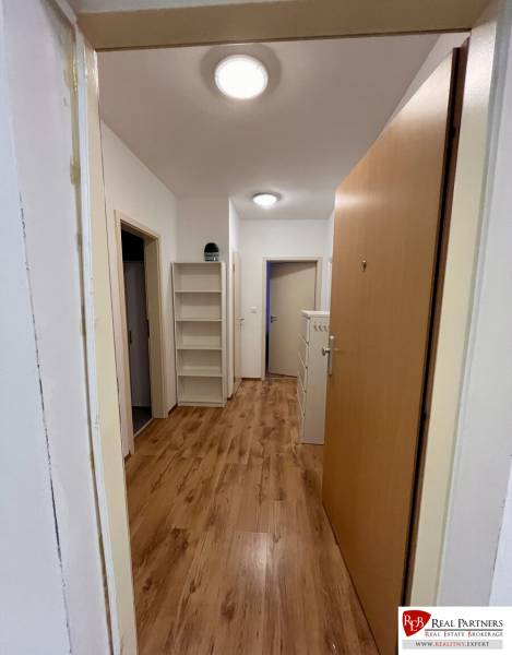 Flur in einer 2-Zimmer-Wohnung mit Holzboden und Regalen an der Wand.