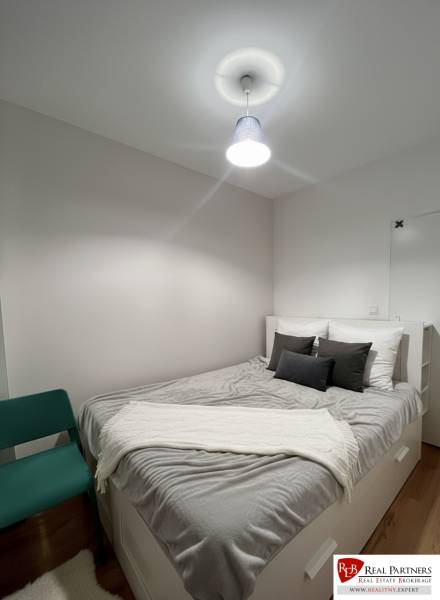 Schlafzimmer in einer 2-Zimmer-Wohnung mit weißen Möbeln, grauen Accessoires und einem Sessel.