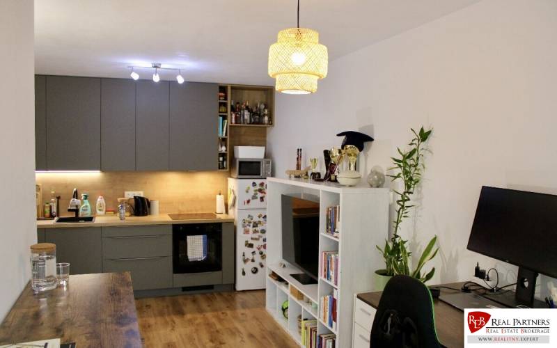 Zweizimmerwohnung mit Küche, Wohnzimmermöbel, Computertisch und Boden mit Holzdekor.