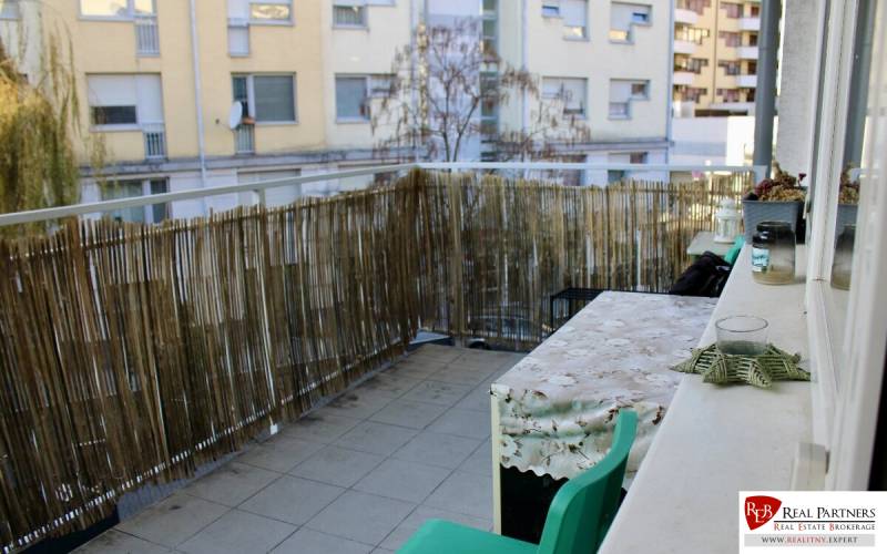 Der Balkon mit einem Rattanzaun und einem Tisch gehört zu einer 2-Zimmer-Wohnung.