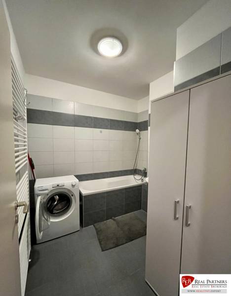 Badezimmer mit Waschmaschine, Badewanne und weißen Fliesen in einer 2-Zimmer-Wohnung.