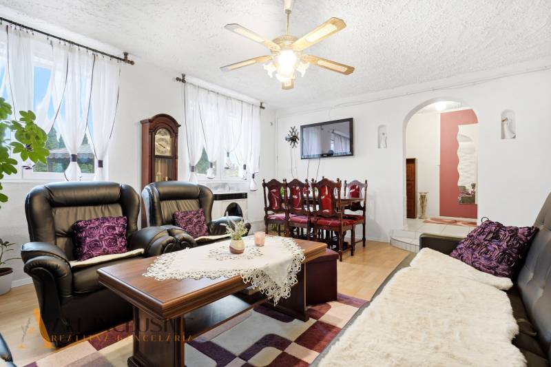 Wohnzimmer eines Einfamilienhauses mit Kamin, schwarzen Sofas und einem Boden in Holzoptik.