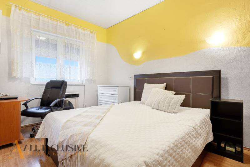 Schlafzimmer im Einfamilienhaus mit Bett, Sessel und Boden in Holzoptik.