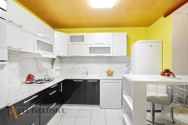 Eine Küche in einem Einfamilienhaus mit hellen Schränken, Marmorverkleidung und weißen Geräten.