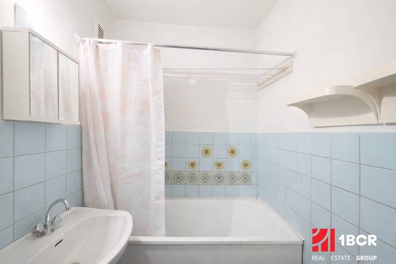 Badezimmer in einer Einzimmerwohnung mit Badewanne, Waschbecken und hellblauen Fliesen.