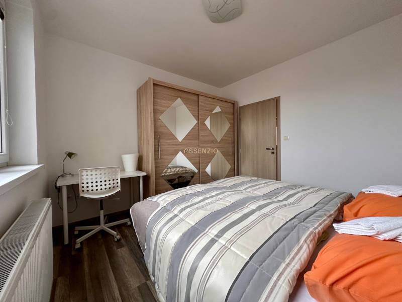 Schlafzimmer in einer 3-Zimmer-Wohnung mit Bett, Schrank, Tisch und Boden in Holzoptik.