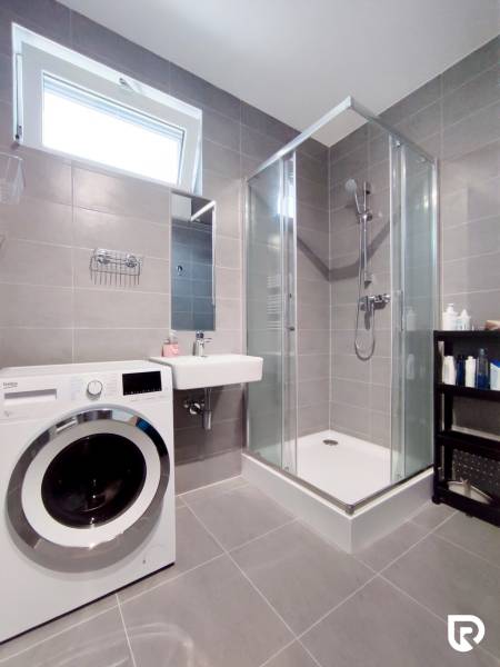 Badezimmer in einer 3-Zimmer-Wohnung mit Waschmaschine, Duschkabine und Waschbecken.