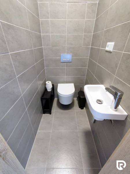 Badezimmer mit Wandtoilette, Waschbecken und grauen Fliesen in einer 3-Zimmer-Wohnung.