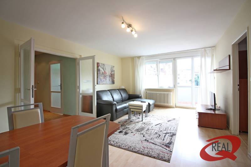 Wohnzimmer in einer 3-Zimmer-Wohnung mit Holzboden und schwarzem Sofa.