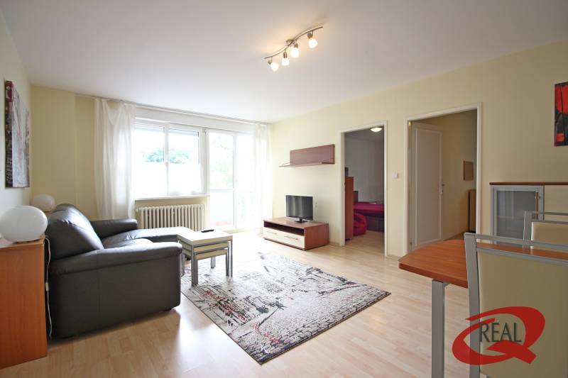 Wohnzimmer einer 3-Zimmer-Wohnung mit Sofa, Tisch und Fernseher auf einem Boden mit Holzdekor.