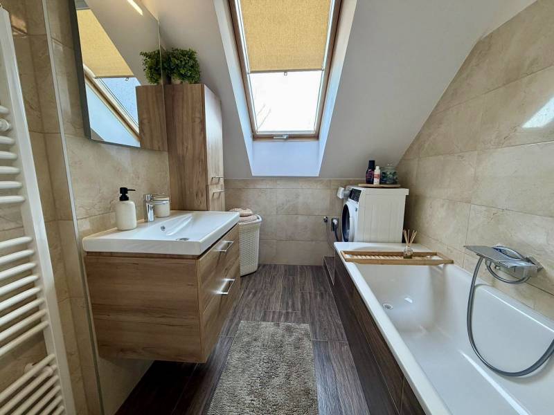Ein Badezimmer in einer 2-Zimmer-Wohnung mit Holzboden, Badewanne und Dachfenster.