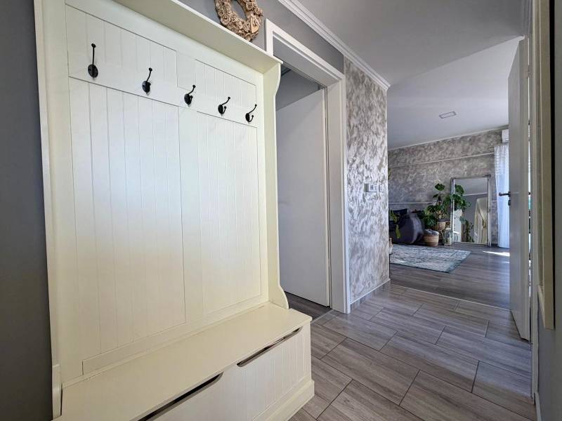 Eingangsflur in einer 2-Zimmer-Wohnung mit Kleiderhaken, der in das Wohnzimmer mit Pflanzen führt.