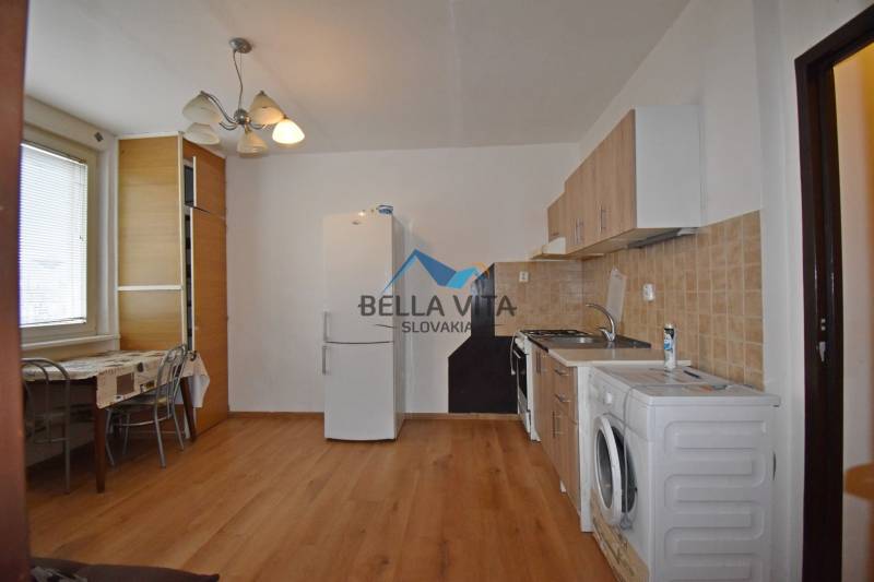 Küche in einer Einzimmerwohnung mit Holzboden, Esstisch und Geräten.