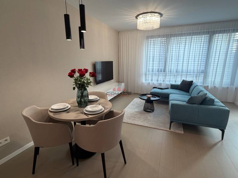 Wohnzimmer in einer Zweizimmerwohnung mit grauem Sofa, Esstisch und Boden in Holzoptik.