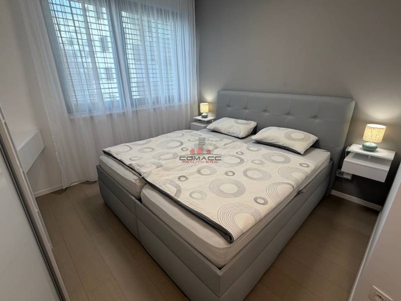 Schlafzimmer in einer 2-Zimmer-Wohnung mit Bett, Nachttischen und Boden mit Holzdekor.