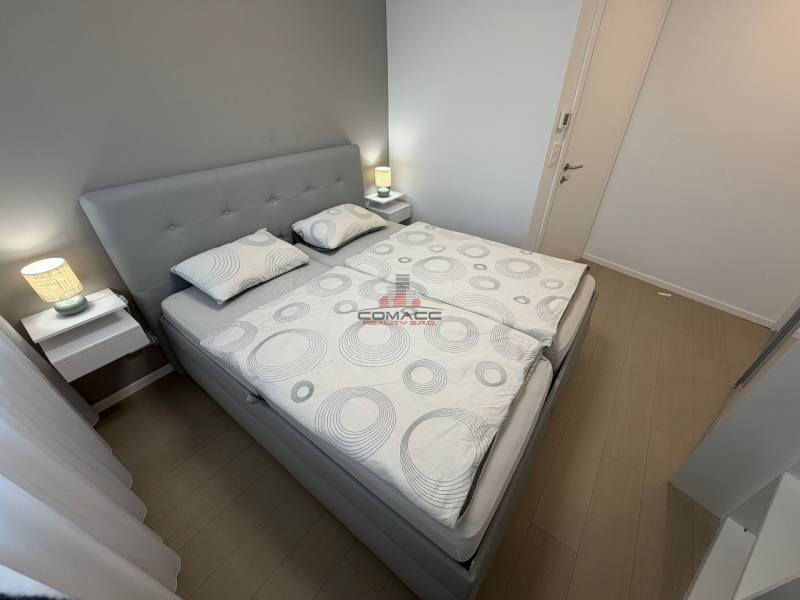 Schlafzimmer mit Doppelbett und Holzboden in einer Zweizimmerwohnung.