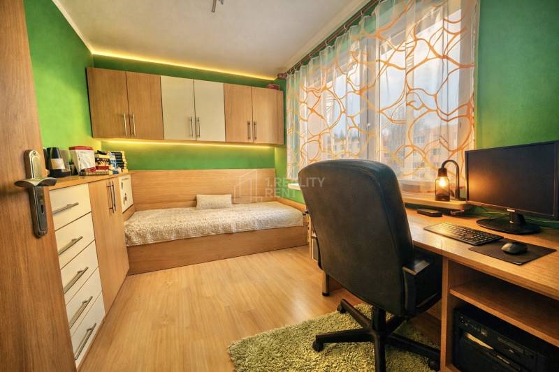 Ein Zimmer in einer 4-Zimmer-Wohnung mit einem Schreibtisch, einem Bett und einem Boden in Holzoptik.