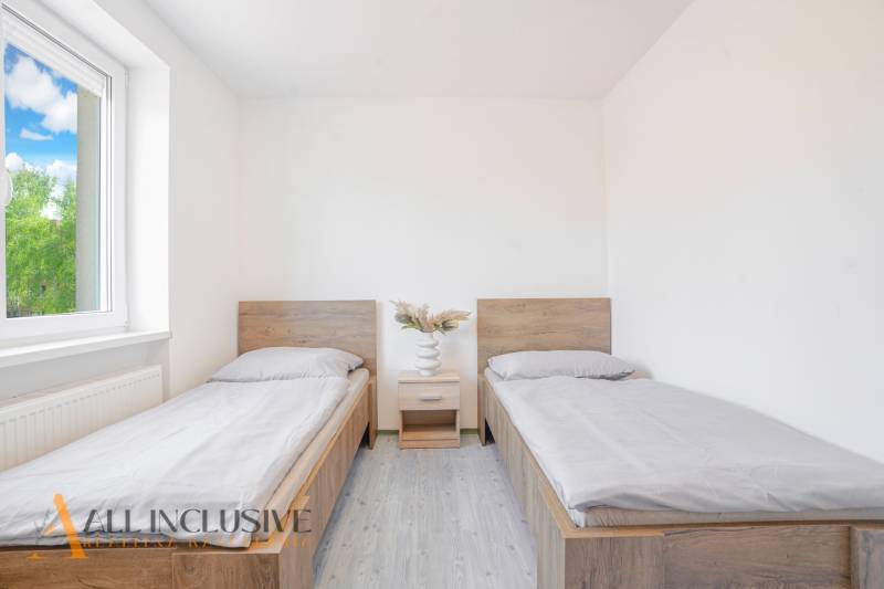 Ein Zimmer mit zwei Betten, einem Nachttisch und einem Boden in Holzoptik.