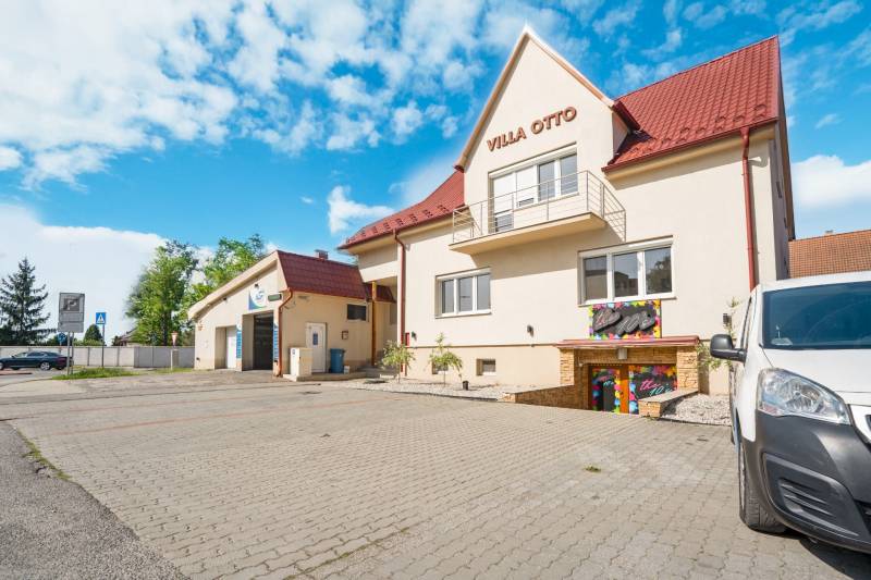 Das Gebäude in der Villa Otto in Dunajská Streda mit rotem Dach und gepflastertem Parkplatz.