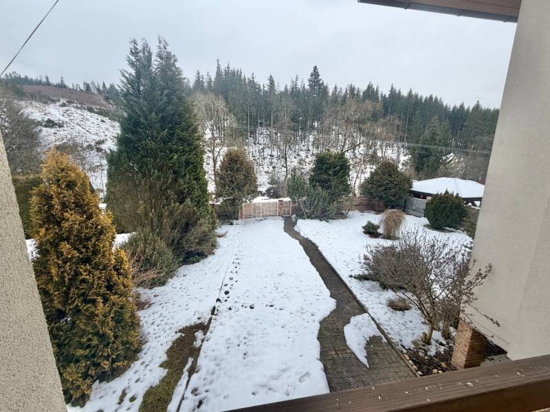 Ein verschneiter Garten eines Einfamilienhauses in Čadca in der Straße Čadečka mit Nadelbäumen und Rasen.