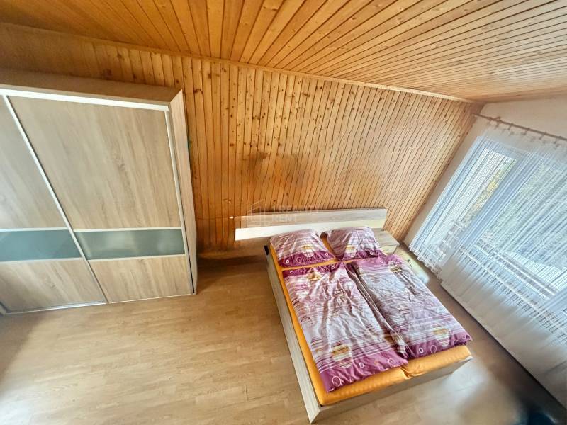Schlafzimmer im Einfamilienhaus mit Holzverkleidung, Boden mit Holzdekor, großes Fenster.