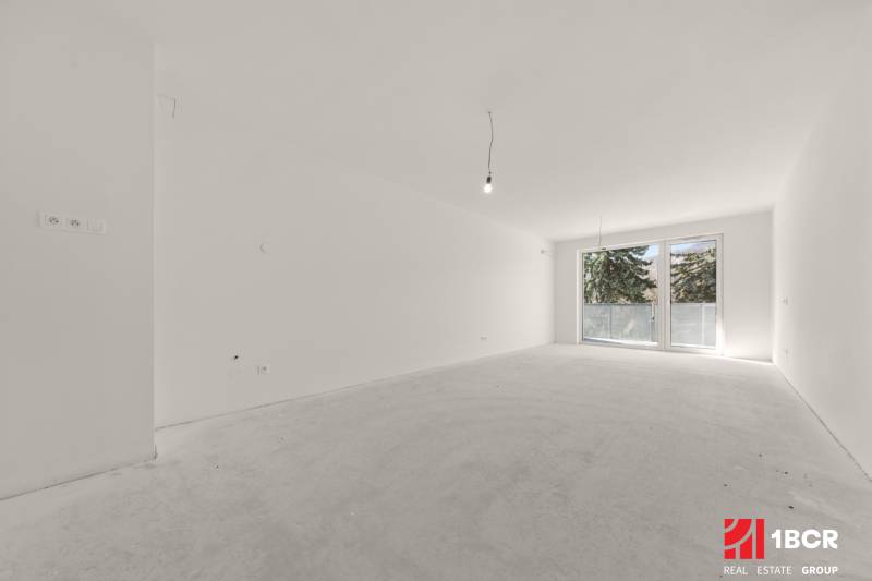 Ein geräumiges Zimmer in einer 4-Zimmer-Wohnung mit einem großen französischen Fenster und weißen Wänden.