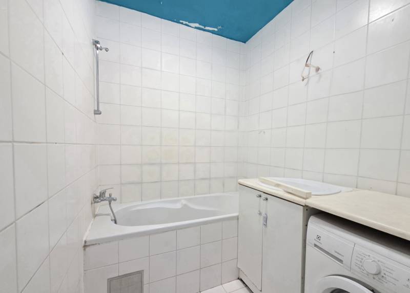 Badezimmer in einer 2-Zimmer-Wohnung mit Badewanne, weißen Fliesen und Waschmaschine.