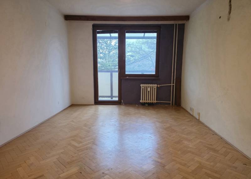 Ein Zimmer mit Holzboden, einem großen Fenster und einem Heizkörper in einer 2-Zimmer-Wohnung.