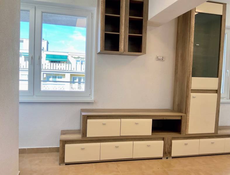 Wohnwand in einer Einzimmerwohnung mit Holzboden und Blick aus dem Fenster.