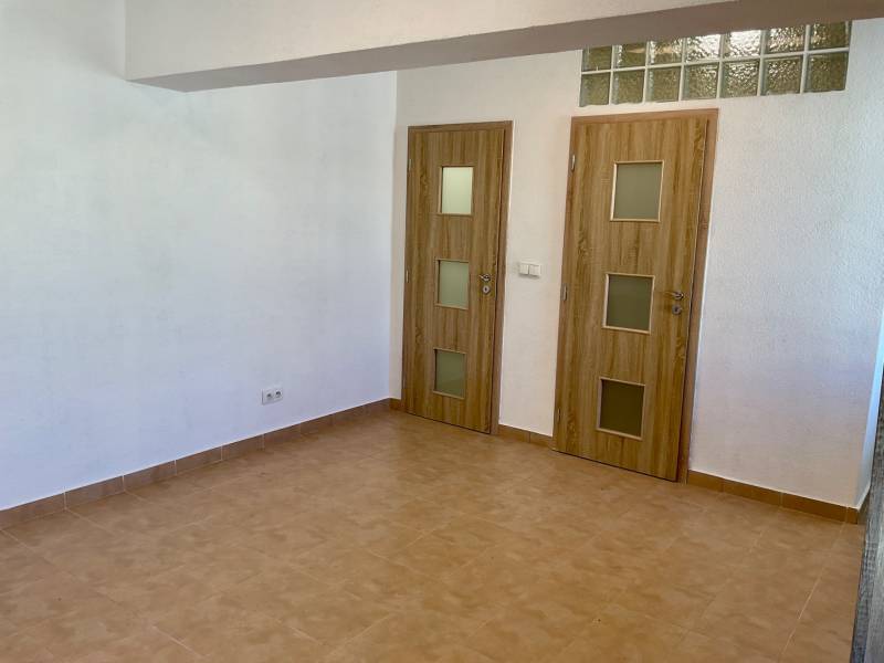 Innenraum einer Einzimmerwohnung mit Keramikboden und zwei Türen mit Holzdekor.