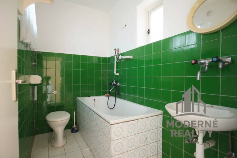 Ein Badezimmer in einem Einfamilienhaus mit grünen Fliesen und einer klassischen Badewanne.