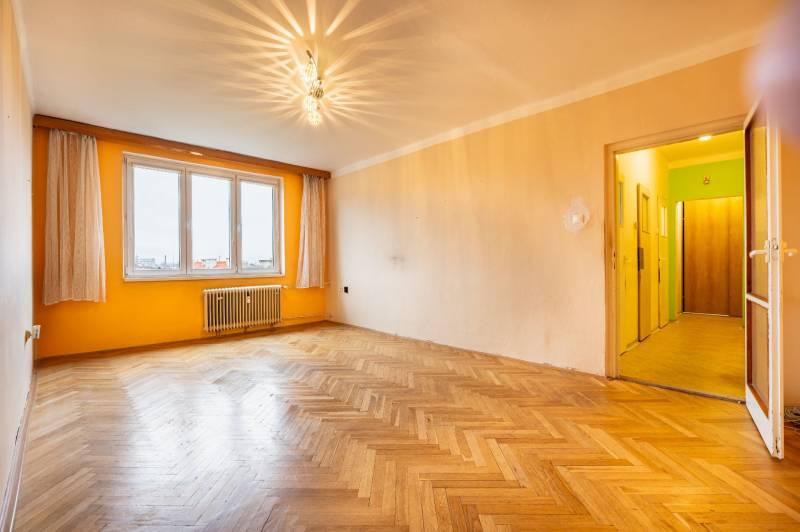 Ein geräumiges Zimmer mit Holzboden und einer orangefarbenen Wand in einer Zweizimmerwohnung.