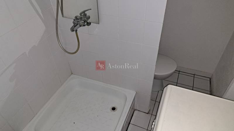 Badezimmer in einer Einzimmerwohnung mit weißen Fliesen und einer Duschkabine.