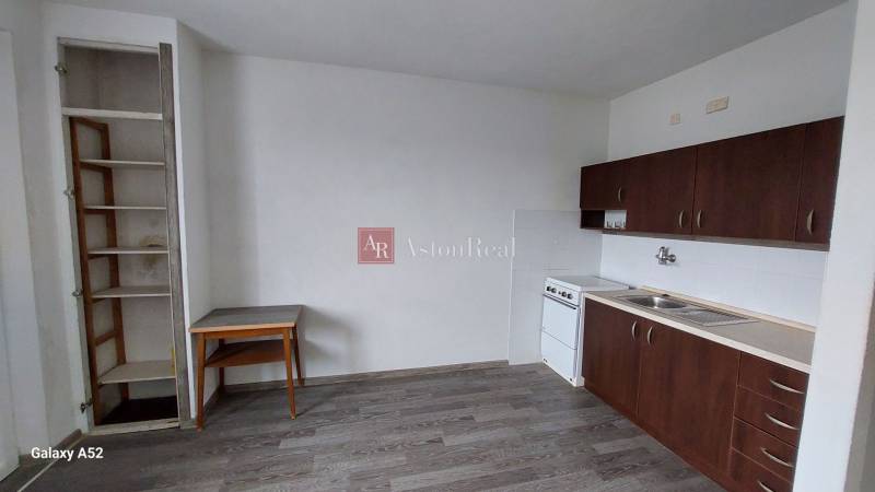 Küche in einer Einzimmerwohnung mit dunklen Schränken und einem Boden in Holzoptik.