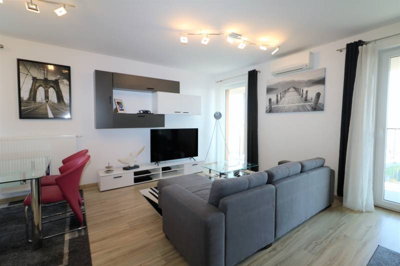 Wohnzimmer in einer 2-Zimmer-Wohnung mit Sofa, Fernseher und Boden in Holzoptik.