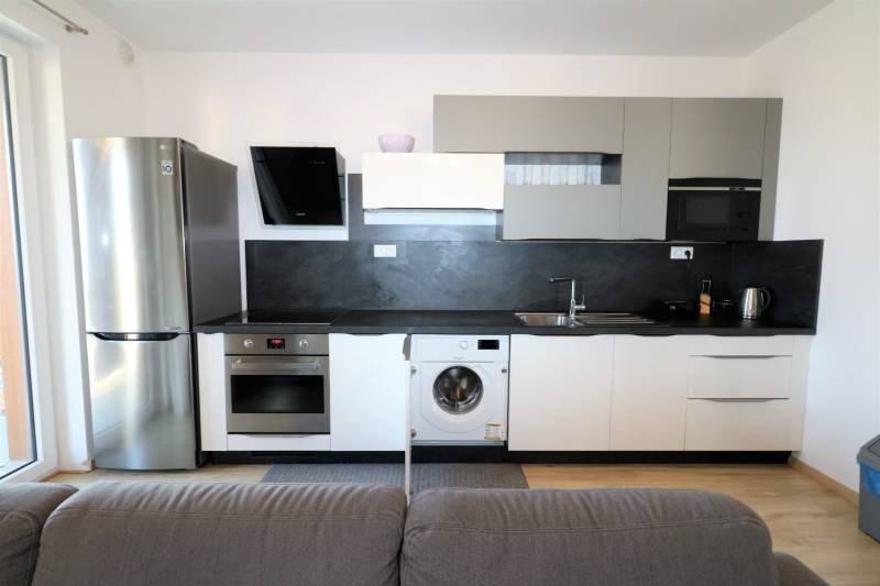 Küche in einer 2-Zimmer-Wohnung mit grauen Schränken, Geräten und einem Boden in Holzoptik.