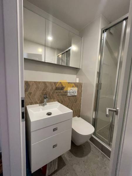 Badezimmer in einer Einzimmerwohnung mit Waschbecken, Duschkabine und Spiegelschrank.