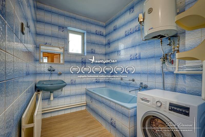 Badezimmer mit Dusche und Waschmaschine in einem Einfamilienhaus. Blaue Fliesen und ein weißer Boiler.