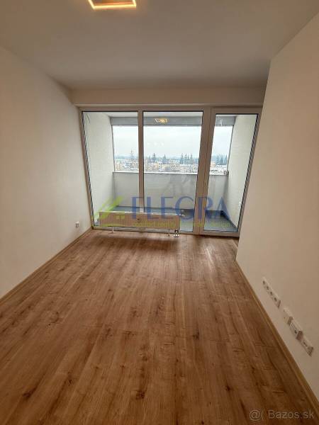 Wohnzimmer in einer Einzimmerwohnung mit Holzboden und großen Fenstern.