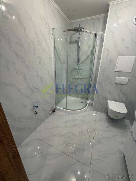 Badezimmer mit Marmorkacheln und Duschkabine in einer Einzimmerwohnung.